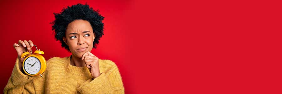 African American woman holding clock on red background